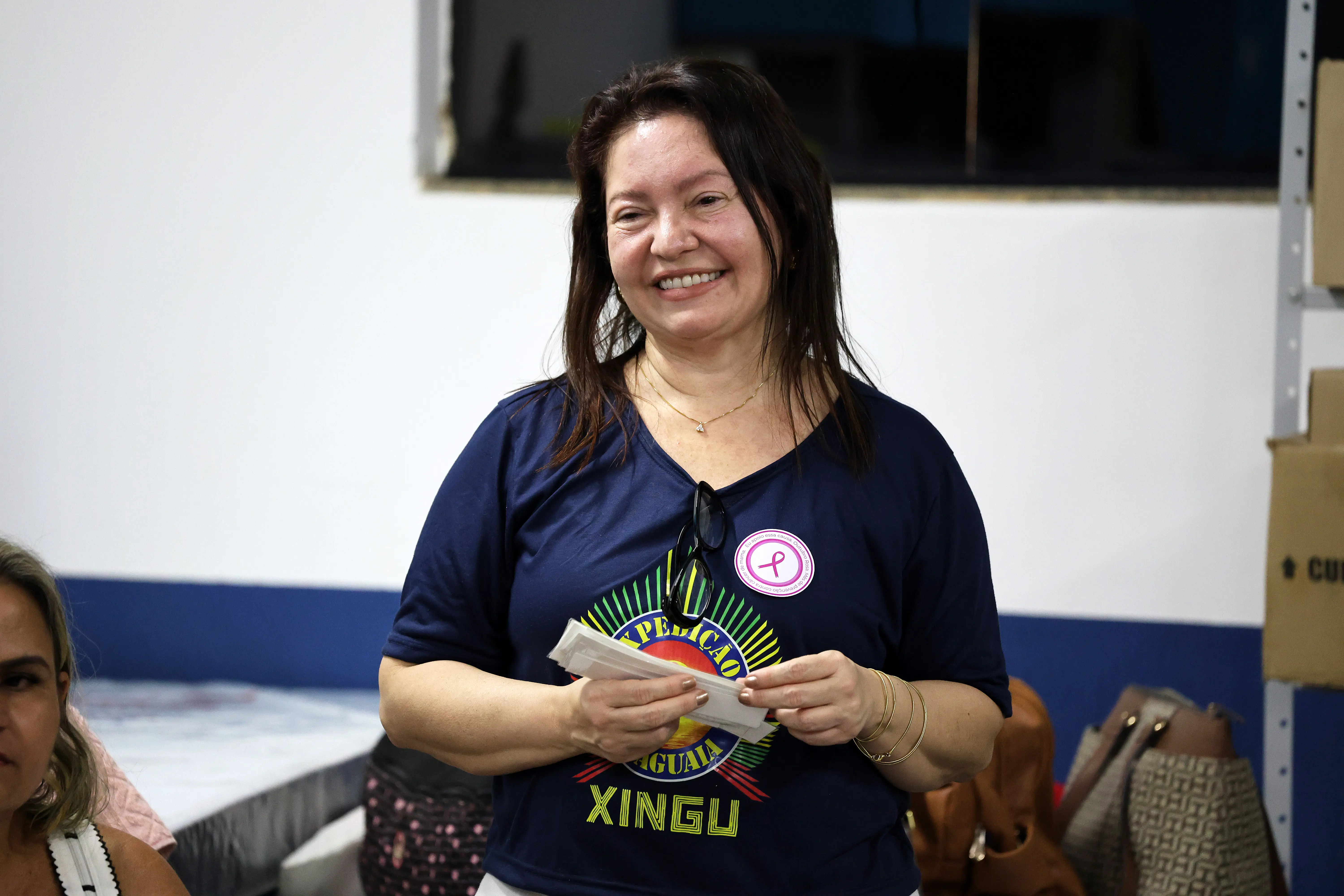 Pessoa sorridente com papéis na mão; durante encontro grupal. Sala organizada, atmosfera leve e engajada.