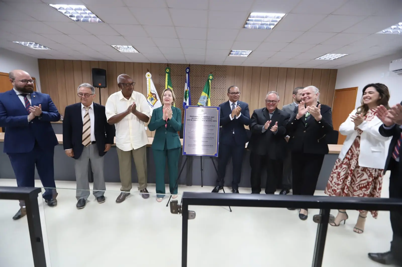 foto colorida em ângulo aberto. a presidente e demais autoridades estão em pé, ao lado da placa de inauguração, dentro do Tribunal do Júri, no Fórum de Alto Garças