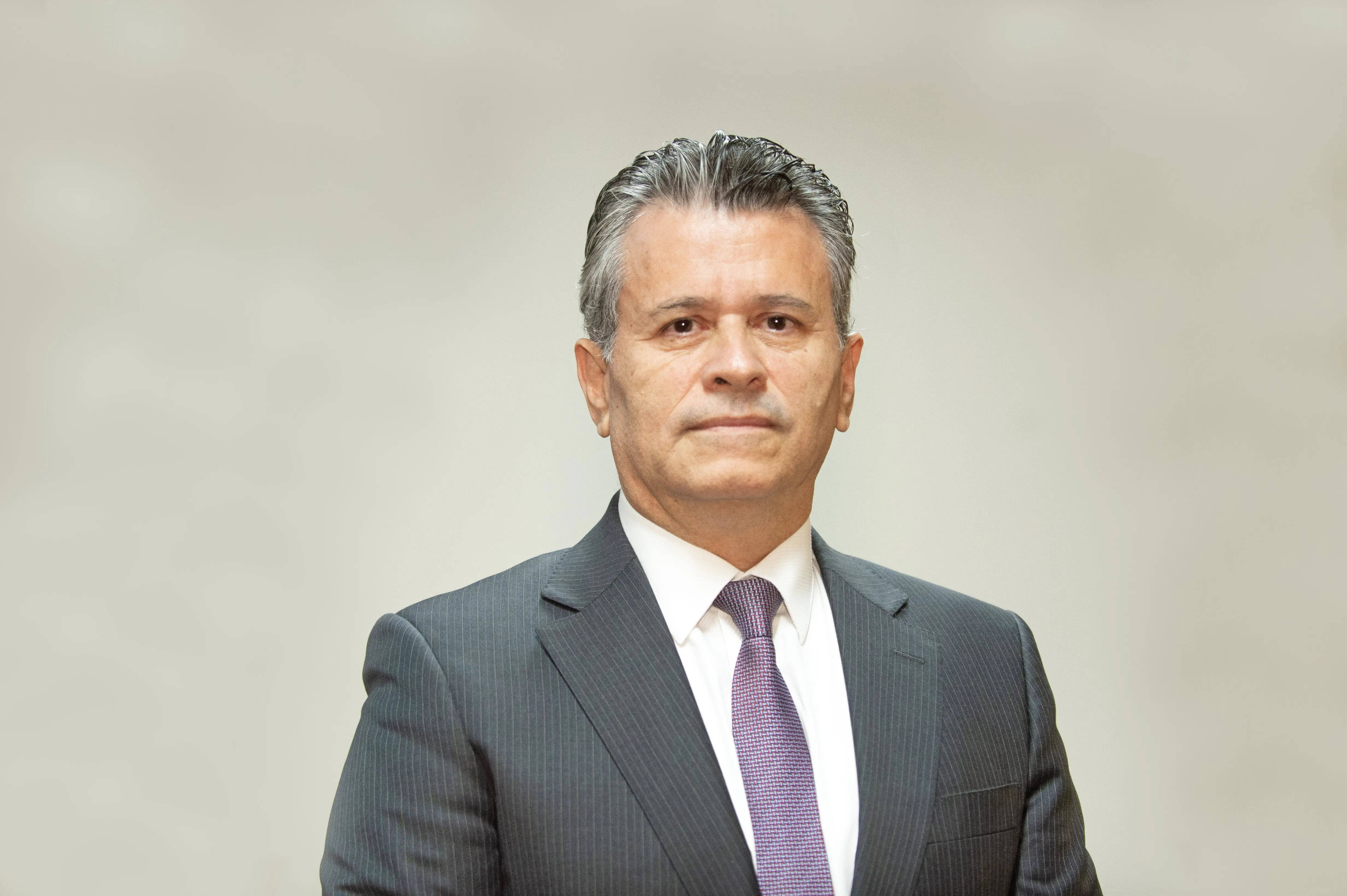 Foto de busto do juiz Jones Gattass Dias posando para a foto. ele é um homem branco, de cabelos grisalhos, olhos escuros, usando camisa branca, gravata lilás e paletó cinza.