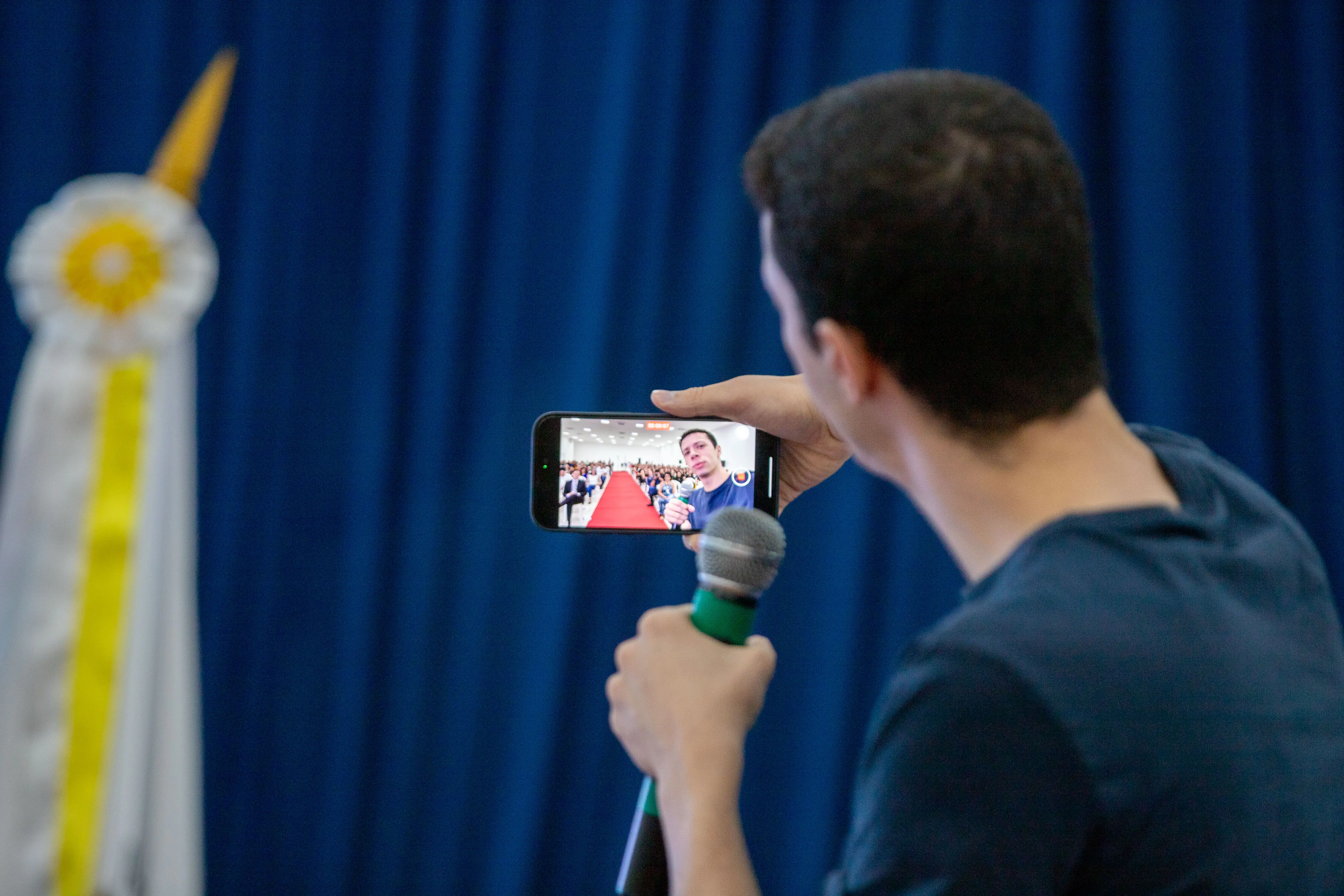 Foto em ângulo fechado de Nicolas que aparece de costas segurando celualr fazendo uma selfie. Ele faz palestra durante o TJMT Inclusivo, em Sorriso