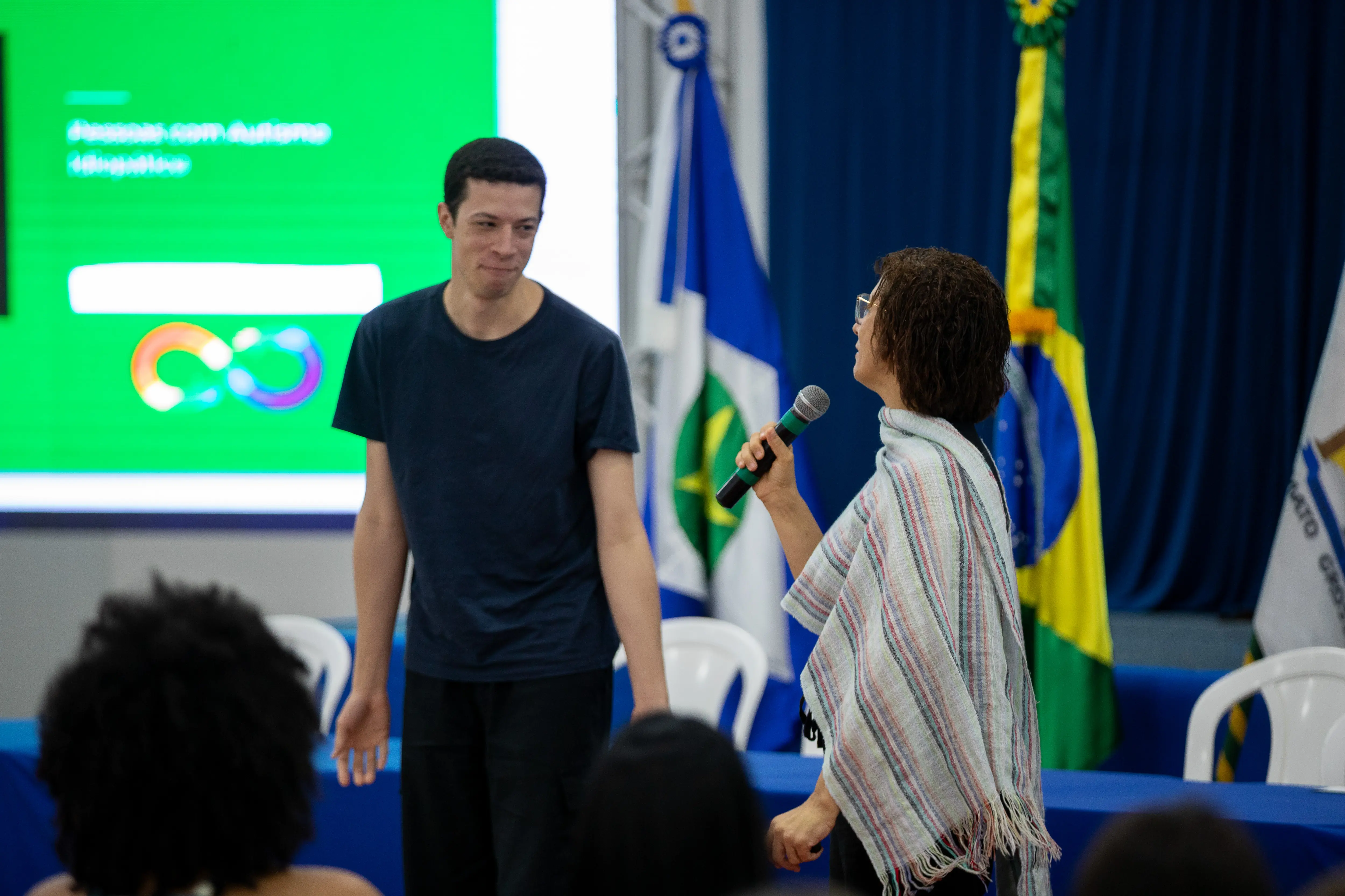 Foto em ângulo fechado de Nicolas com sua mãe, durante o TJMT Inclusivo, em Sinop
