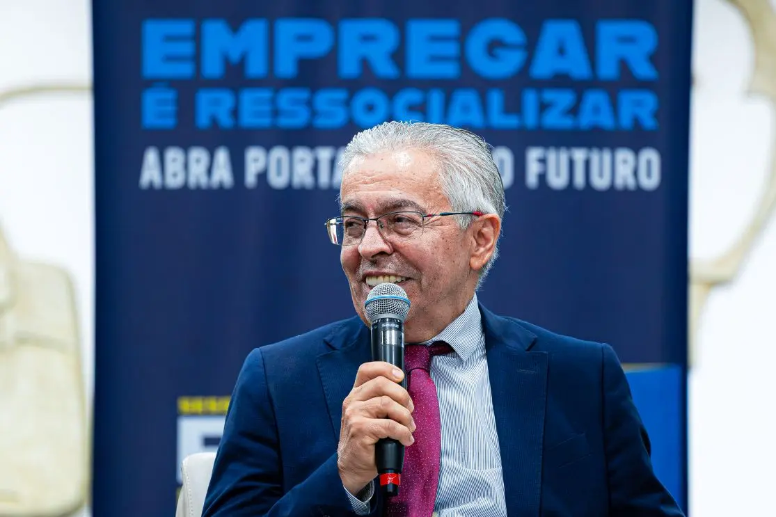 Foto horizontal que mostra o presidente do TRT-MT, desembargador Aguimar Peixoto, do busto pra cima, falando ao microfone. Ele é um senhor branco, de cabelos brancos, usando camisa azul clara, terno azul marinho, gravata vinho e óculos de grau.