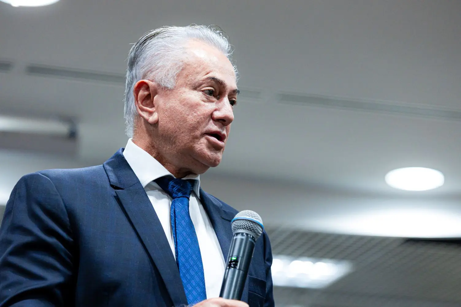Foto horizontal que mostra o desembargador Orlando Perri do busto pra cima, falando ao microfone. ele é um senhor branco, de cabelos brancos, usando camisa branca, gravata azul e terno azul marinho.