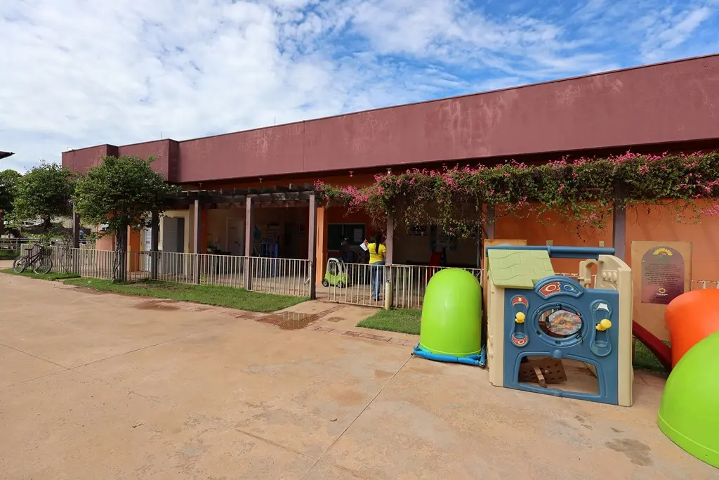 Foto horizontal colorida em plano aberto que mostra a fachada da creche Nina Zaque, com várias flores e brinquedos .