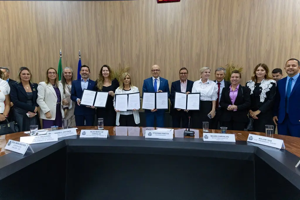 Foto horizontal em plano aberto que mostra várias autoridades de Mato Grosso, dentre elas o governador Otaviano Pivetta e as desembargadoras Nilza Maria Pôssas, Maria Erotides Kneip e Gabriela Knaul, posando em pé par aa foto. Eles seguram e exibem documentos que foram assinados no evento.