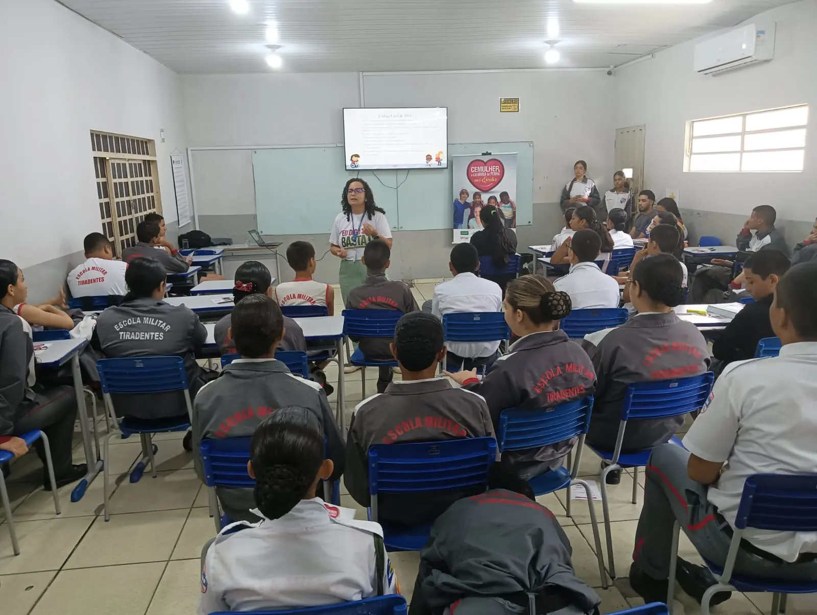 Foto horizontal em plano aberto que mostra uma sala de aula com alunos ouvindo a palestra da servidora Adriany Carvalho, da Cemulher.