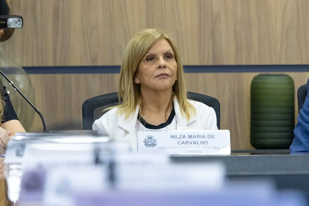 Foto horizontal que mostra a vice-presidente do TJMT, desembargadora Nilza Maria Pôssas de Carvalho, sentada, com um semblante firme. Ela é uma senhora de pele clara, loira, usando vestido e blazer brancos.