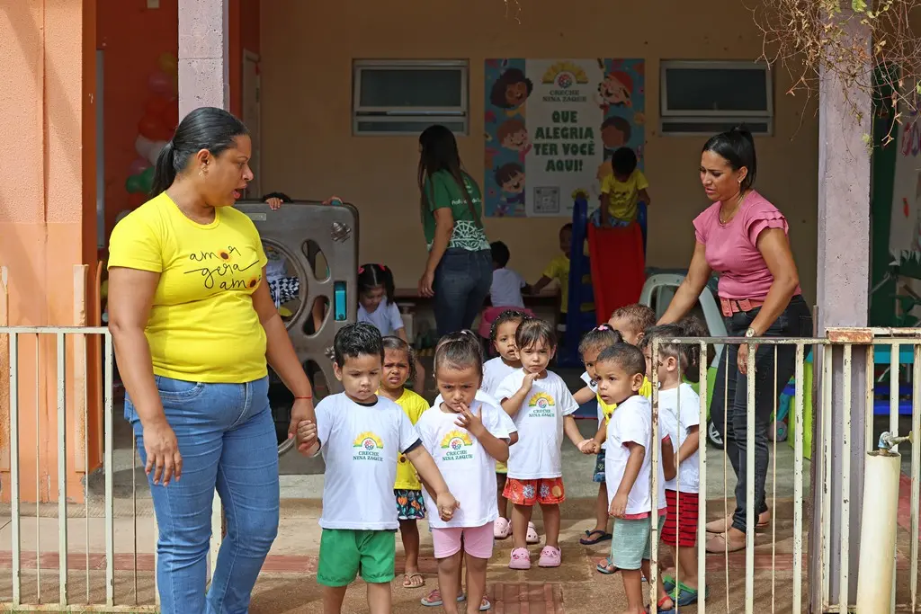 Foto horizontal colorida que mostra professoras conduzindo um grupo de crianças da creche Nina Zaque em fila indiana.