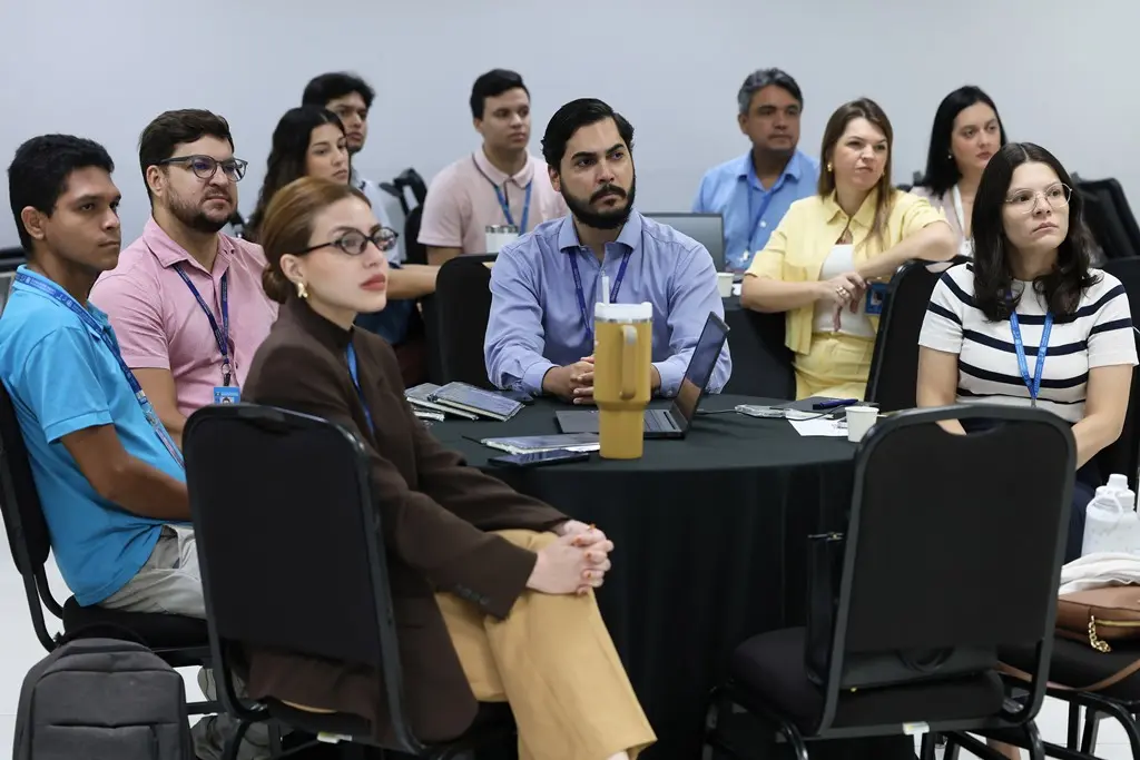 Foto horizontal em plano aberto que mostra 12 servidores do TJMT sentados em volta de mesas redondas, olhando na direção do professor do curso. 