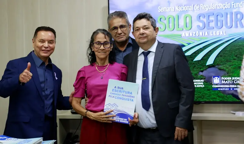 a imagem mostra o corregedor e dois parceiros junto com uma moradora que exibe o título de propriedade.