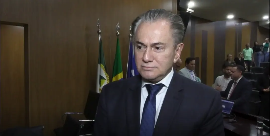 Des. Orlando Perri  é um homem de meia-idade, com cabelos grisalhos penteados para trás, vestindo um terno escuro e gravata azul, olha fixamente para frente. Ao fundo, há bandeiras e pessoas em um auditório.