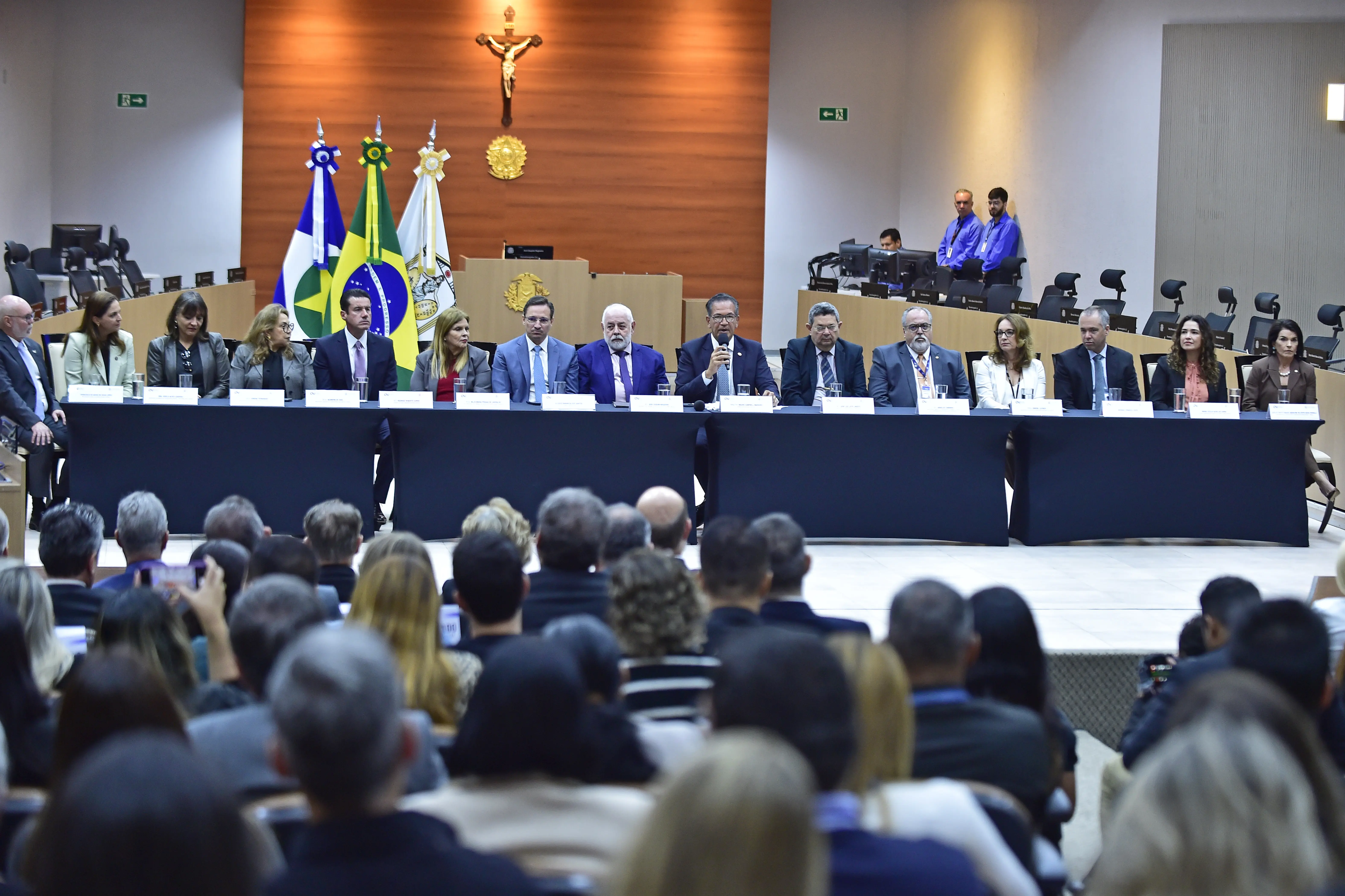Foto em plano aberto que mostra o Plenário 1 do TJMT repleto de pessoas na plateia e, ao centro do Plenário, a mesa de honra composta por autoridades do CNJ, do TJMT e do sistema de justiça estadual. Ao centro está sentado o ministro corregedor Mauro Campbell, falando ao microfone.