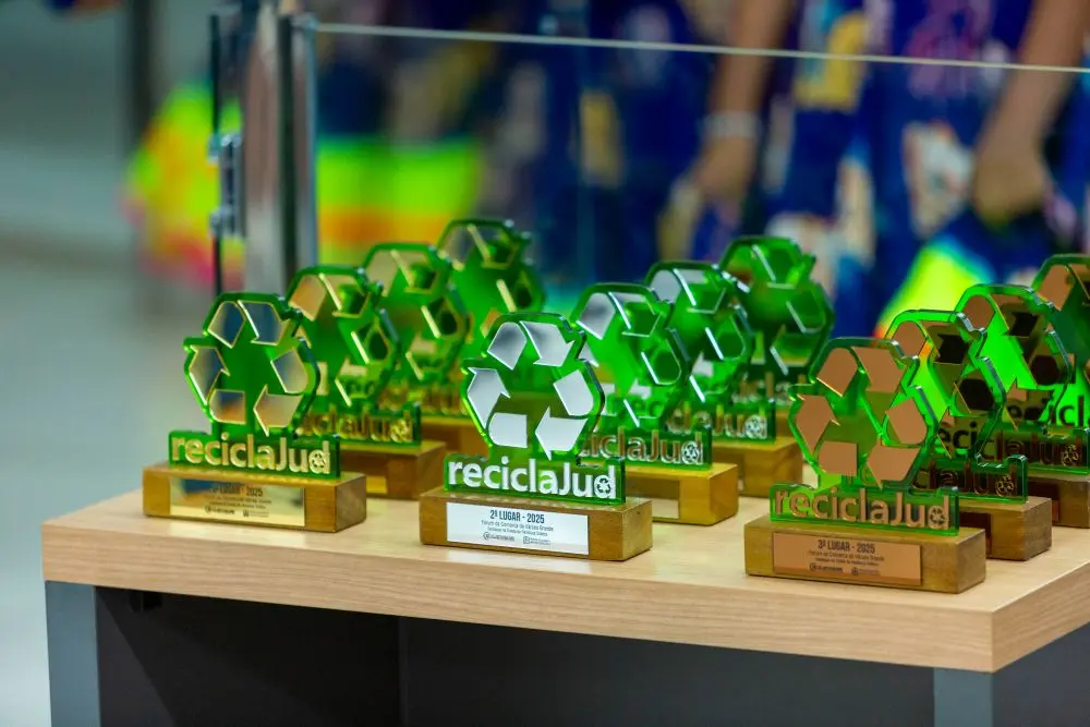 Foto colorida, na horizontal, que mostra uma mesa com vários troféus do Reciclajud. Os troféus são verdes e têm  o símbolo da reciclagem e a palavra ReciclaJud.
