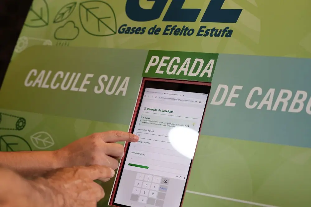 Foto horizontal que mostra detalhe de um totem verde onde está escrito 