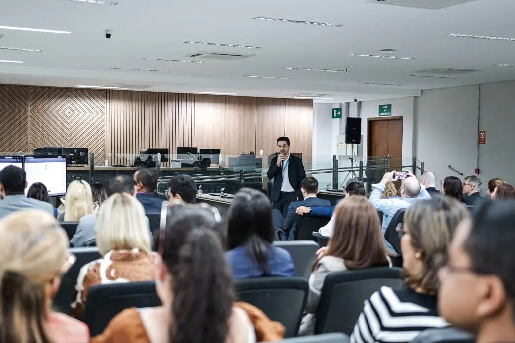 O diretor do DAPI, Guilherme Felipe Schultz, fala ao público durante a entrega no Fórum de Várzea Grande. Em pé, com microfone em mãos, ele se dirige aos magistrados e servidores presentes no auditório, enquanto os participantes acompanham a apresentação sentados.