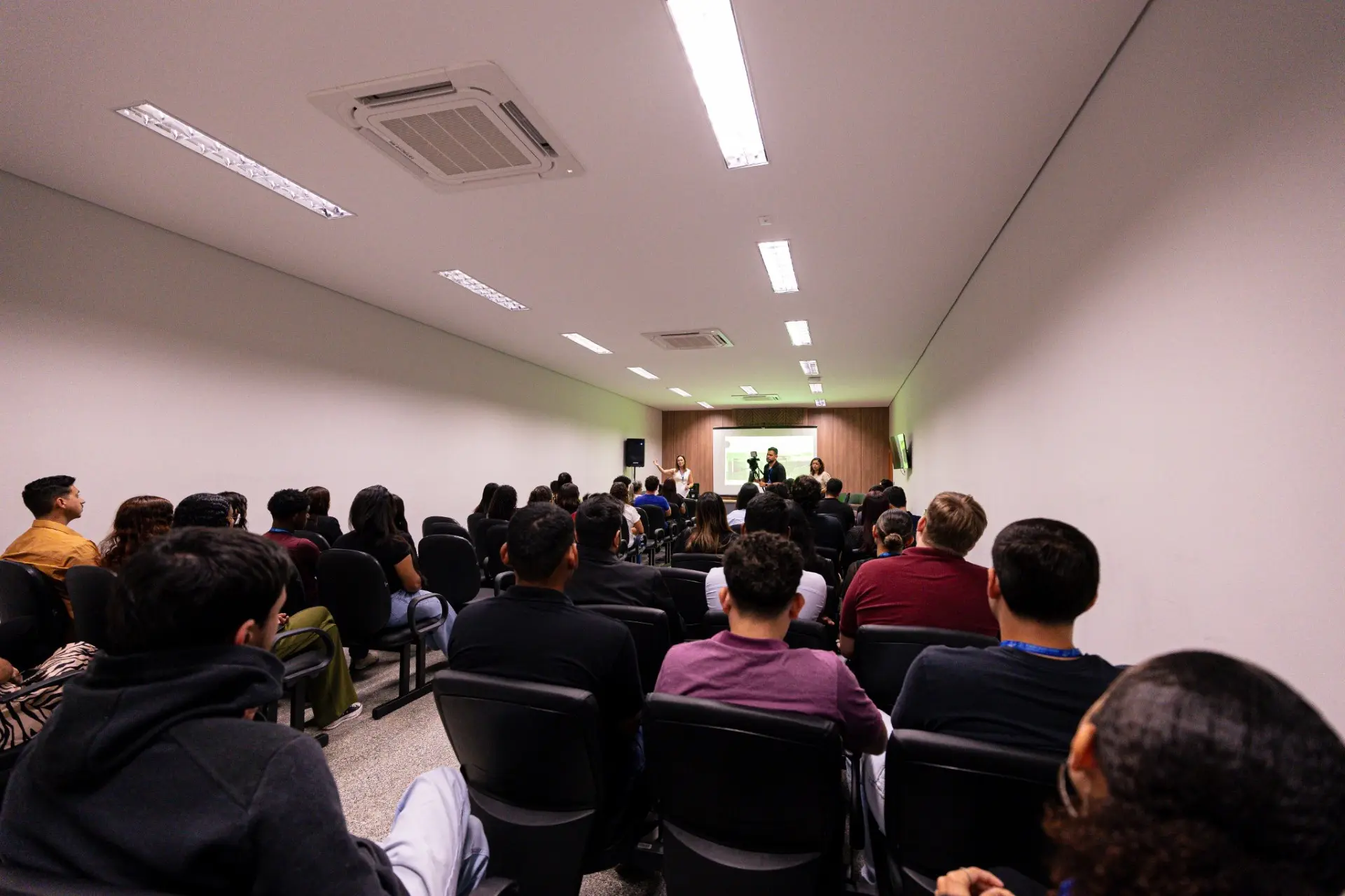 Foto horizontal em plano aberto que mostra um auditório repleto de estagiários do Departamento de Apoio aos Juizados Especiais sentados, de costas para a foto.
