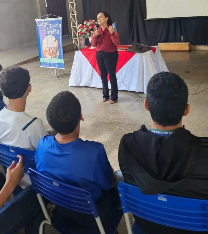 juíza Maria das Graças falando ao microfone de frente para os alunos. 