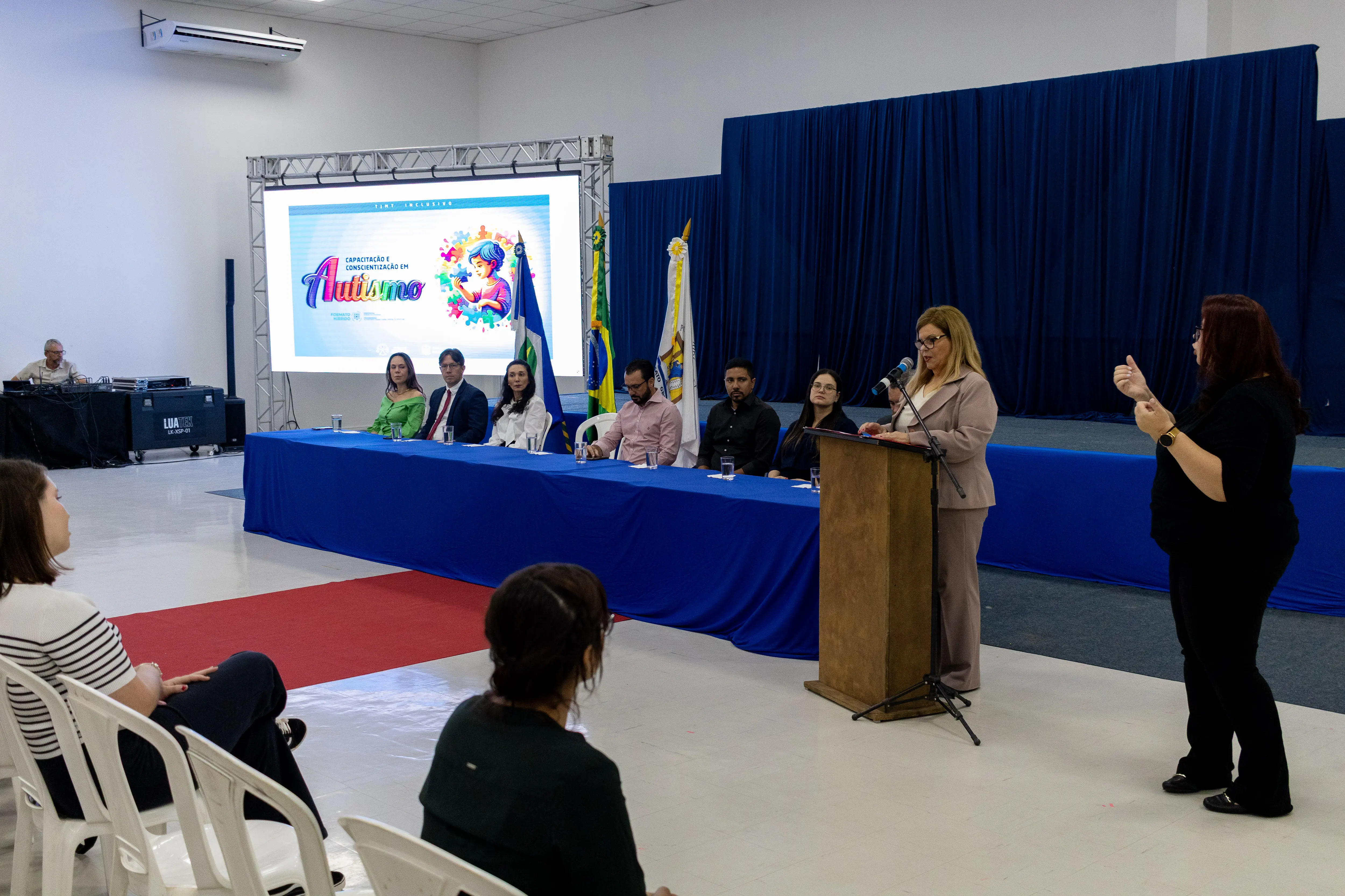 Desembargadora Nilza Pôssas de Carvalho durante o TJMT Inclusivo em Sorriso. Ela fala aos presentes atrás de um púlpito de madeira