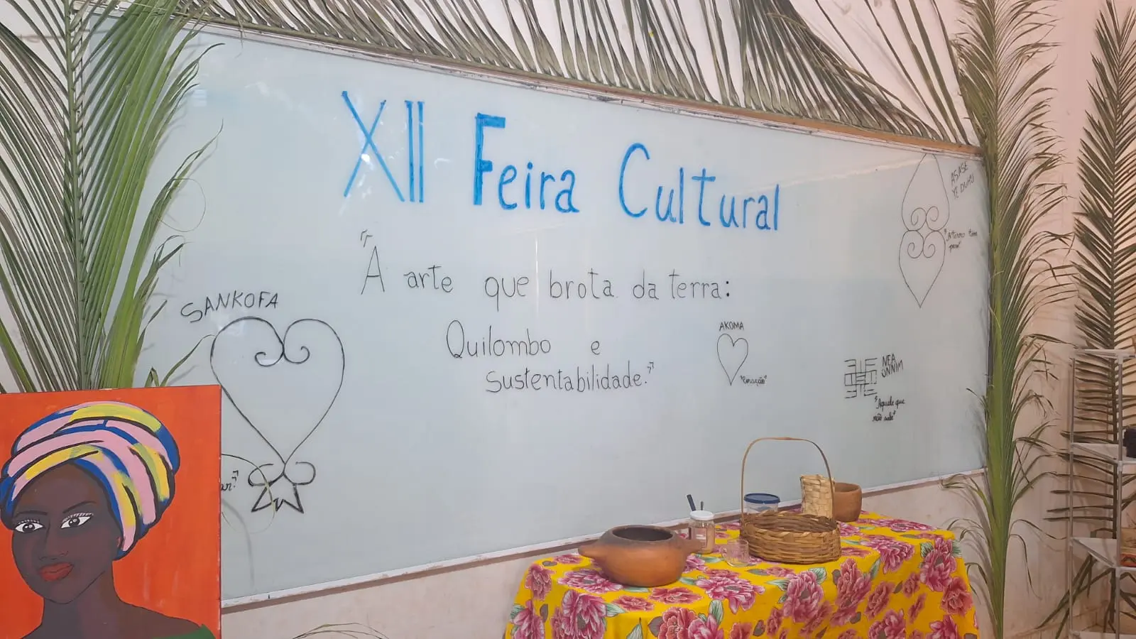 Parede de uma sala de aula decorada para a Feira cultural. A decora��o � composta de pintura de uma mulher negra com turbante, palhas de coqueiro, panos com estampa florida, vasos e cestos. 