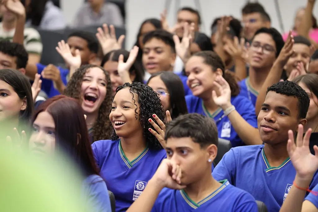 Foto que mostra vários estudantes da Escola Souza Bandeira sorrindo, sentados em poltronas do auditório.