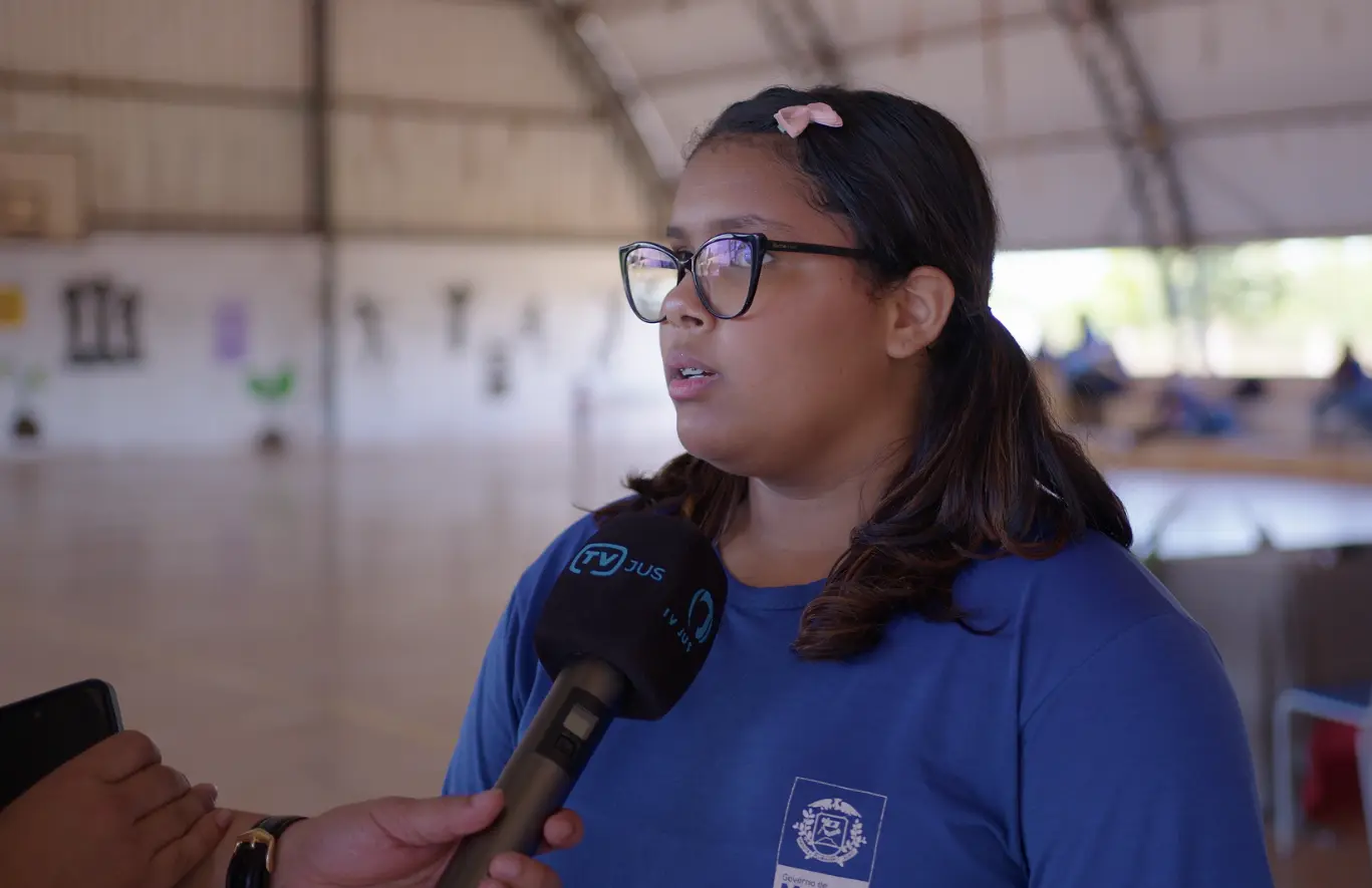 Kamila Hadassa, aluna da escola Ces�rio Neto, durante entrevista � TV Justi�a.  Ela � uma adolescente de pele negra n�o retinta, cabelos pretos e lisos presos em maria-chiquinha com lacinho rosa, usando uniforme azul marinho da escola e �culos de grau.