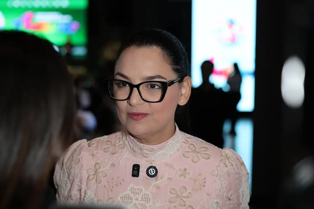 Primeira-dama e vereadora de Cuiabá, Samantha Íris, durante entrevista. Ela é uma mulher branca, de olhos e cabelos castanhos, usando vestido rosa claro florido e óculos de grau de armação preta.