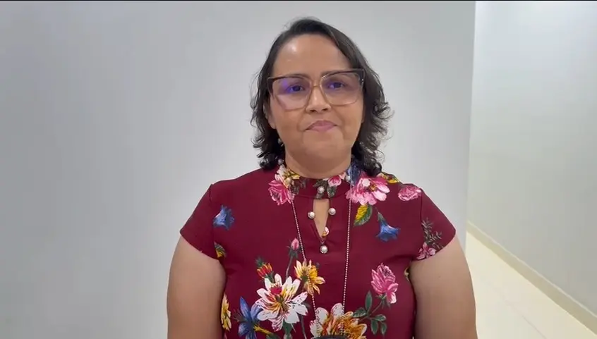 Escrivã Ana Lígia dos Santos posa em área interna clara, usando blusa vinho florida e óculos. Ela olha para a câmera com expressão serena. O fundo neutro reforça o registro oficial realizado durante o evento em Nortelândia.