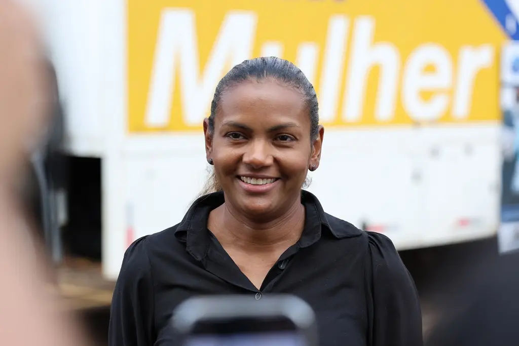 Coordenadora de Saúde do Sesc Mato Grosso, Rosinei Joana, em frente à carreta de Saúde da Mulher, sorrindo. Ela é uma mulher negra, de cabelos castanhos, presos, usando camisa preta. 