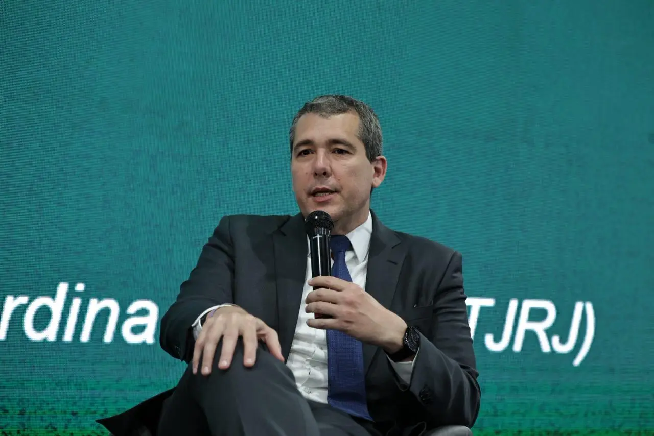 Foto do desembargador Humberto Dalla Bernardina de Pinho. Ele é um homem alto, branco, de cabelos grisalhos, usando camisa branca, gravata azul e terno cinza. Ele está sentado e falando ao microfone.