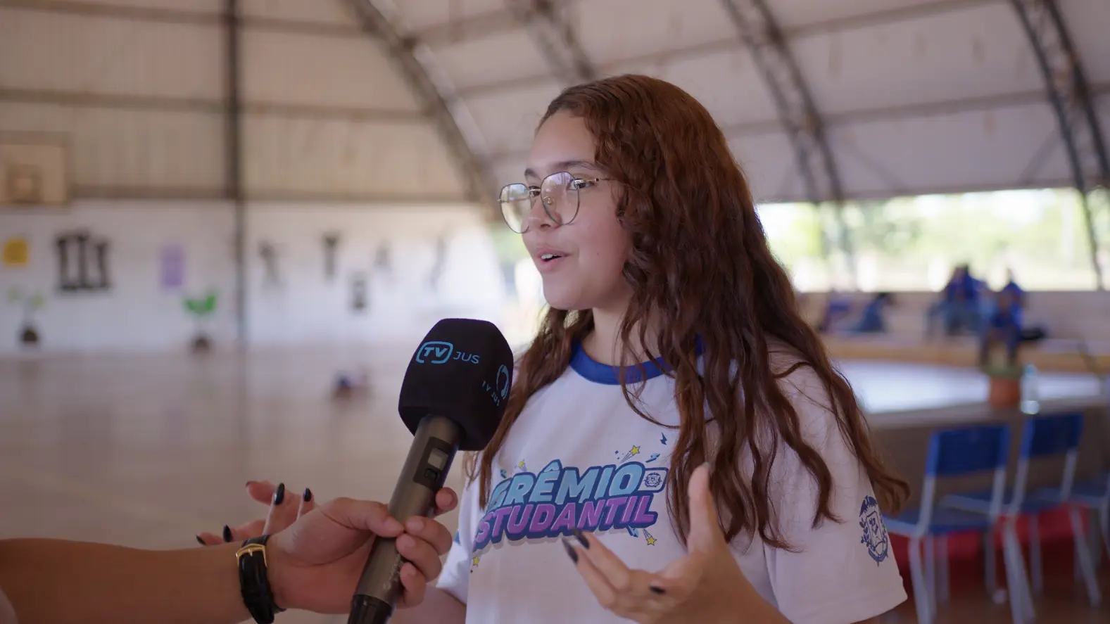 Lorraine Nascimento, aluna da Escola Ces�rio Neto, durante entrevista � TV Justi�a. ela � uma adolescente de pele branca, cabelos longos e ruivos, usando camiseta do gr�mio estudantil e �culos de grau.  