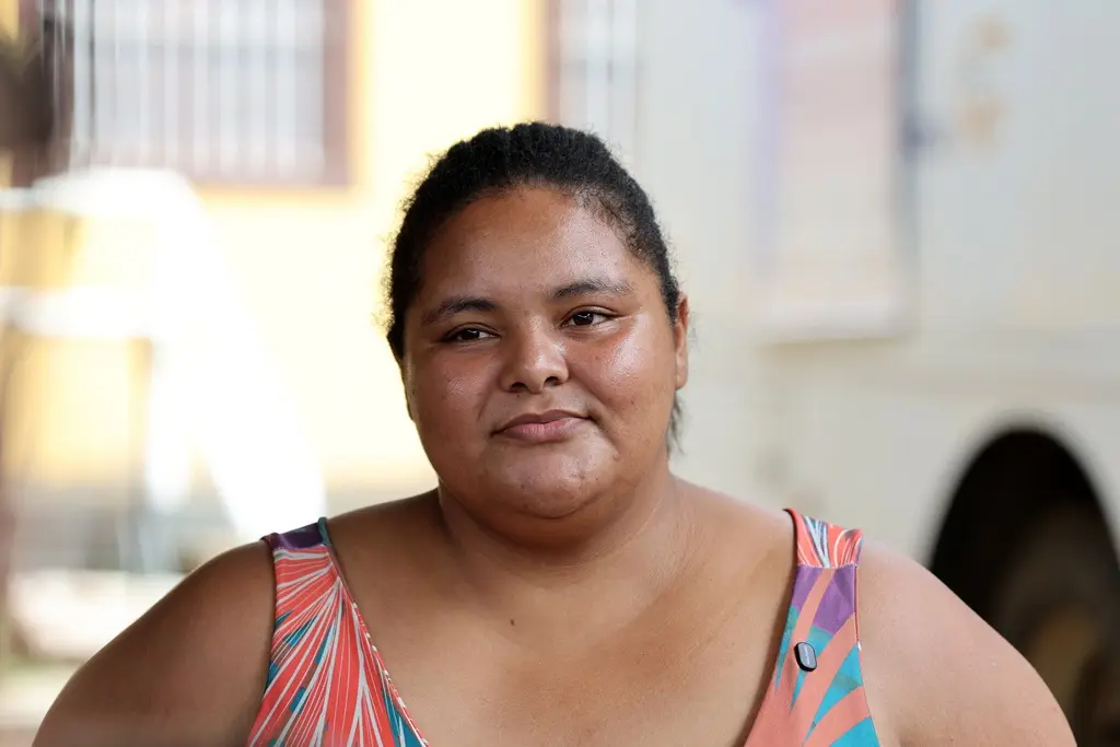 Foto da Elaine Duarte. ela é uma mulher de 30 anos, negra, cabelos castanhos presos, usando um vestido estampado e colorido. 