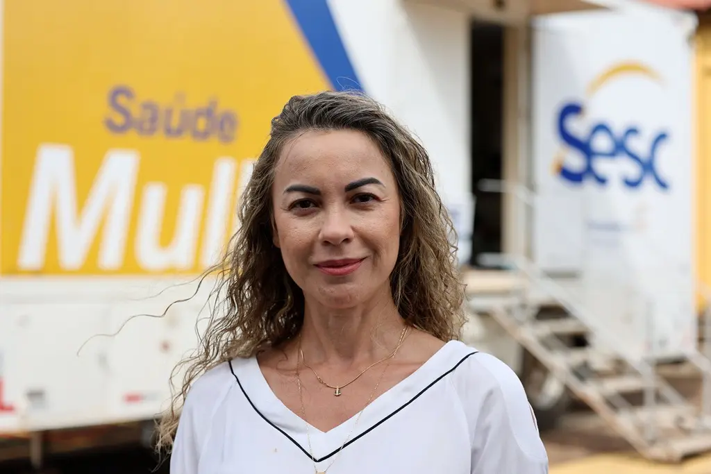 Juíza Cristiane Padim em frente à carreta Saúde da Mulher do Sesc. Ela é uma mulher branca, de cabelos longos, loiros e cacheados, usando uma blusa branca de manga comprida.