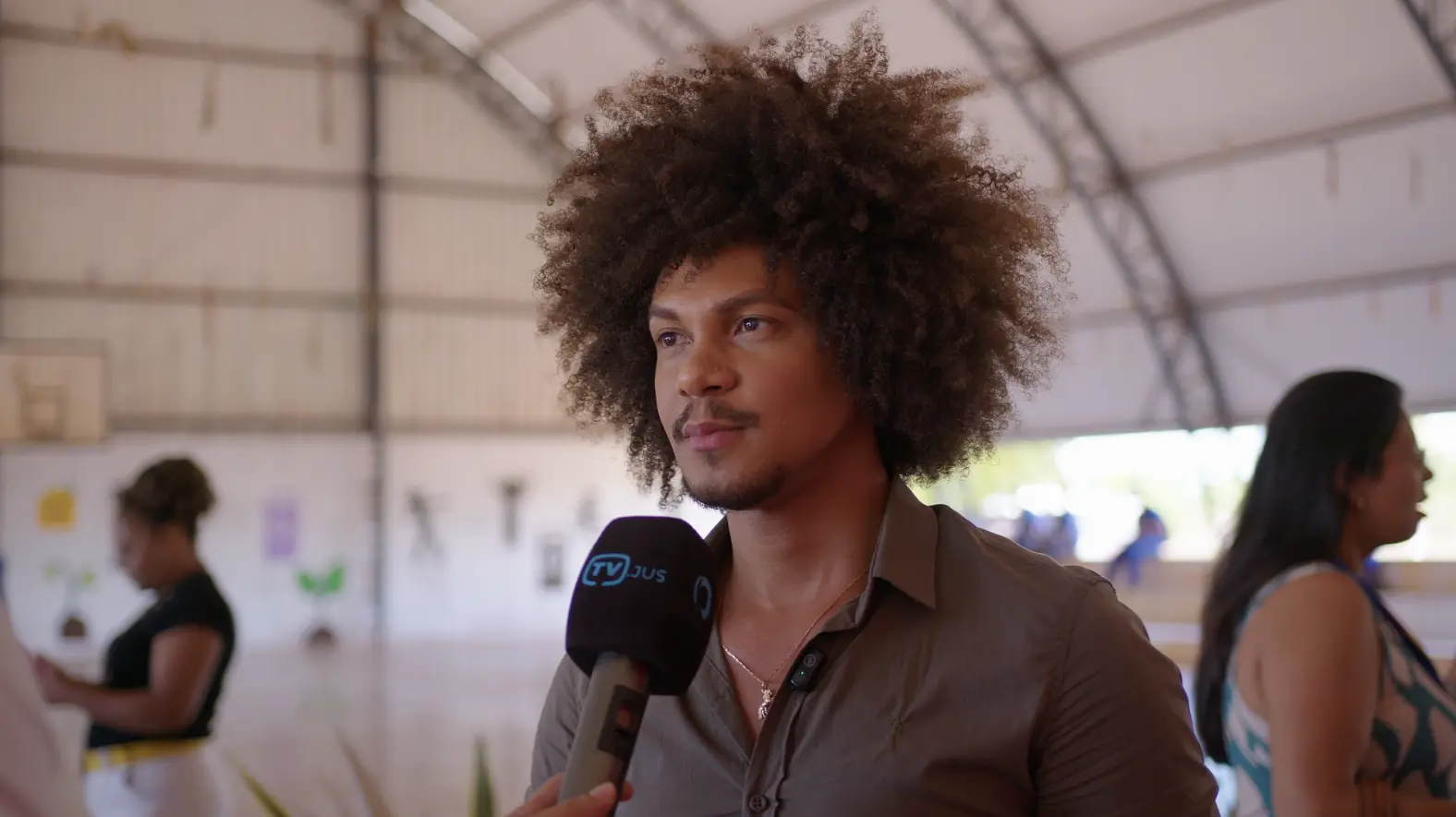 Wagner M�nantha, diretor da Escola Ces�rio Neto, durante entrevista � TV Justi�a. Ele � um homem jovem, negro, de cabelo black power, usando camisa verde militar. Ele est� no gin�sio de uma escola.
