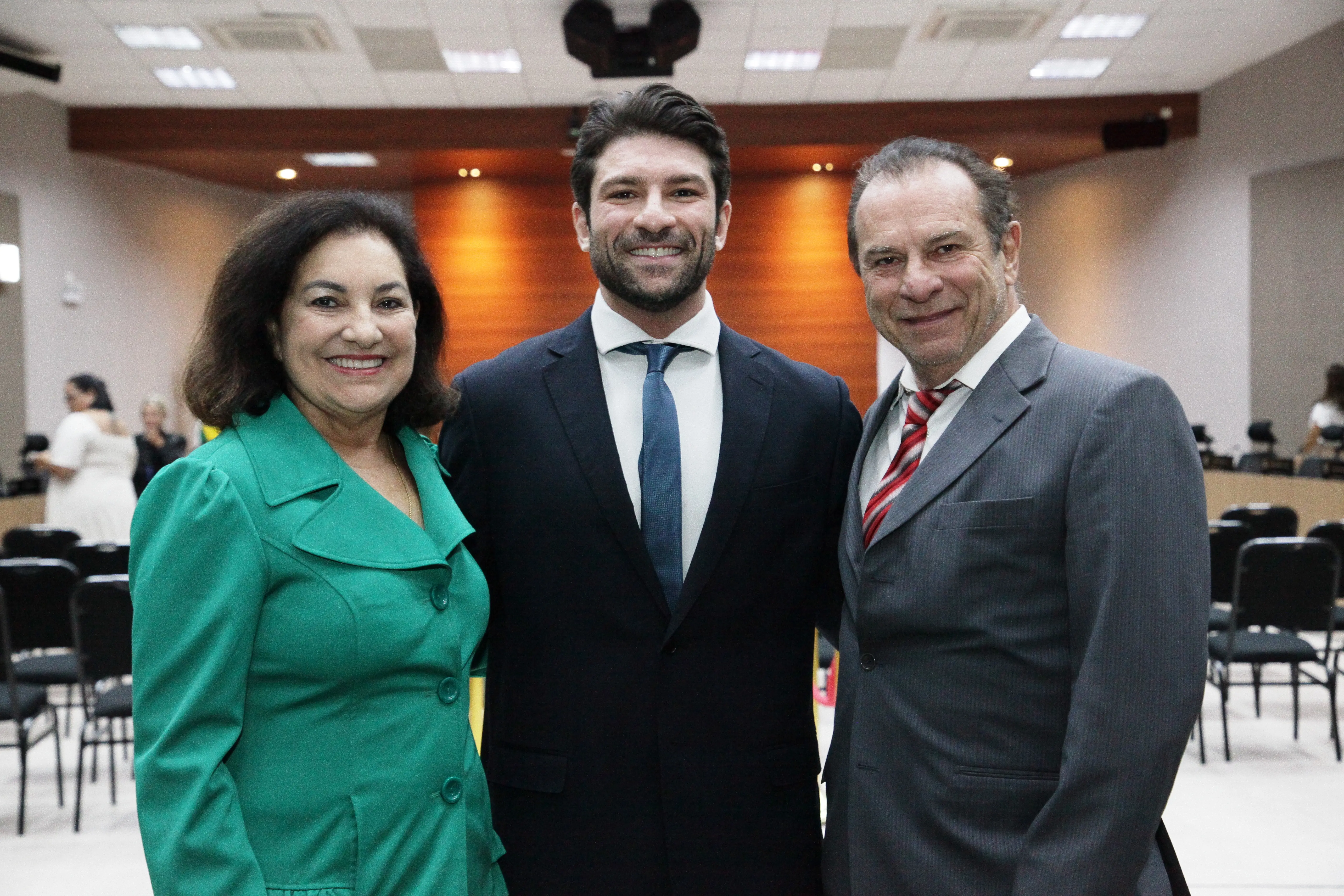 Juiz posa ao lado de familiares no plenário do Tribunal. Todos estão em trajes formais, com cadeiras do colegiado e ambiente institucional visíveis ao fundo.