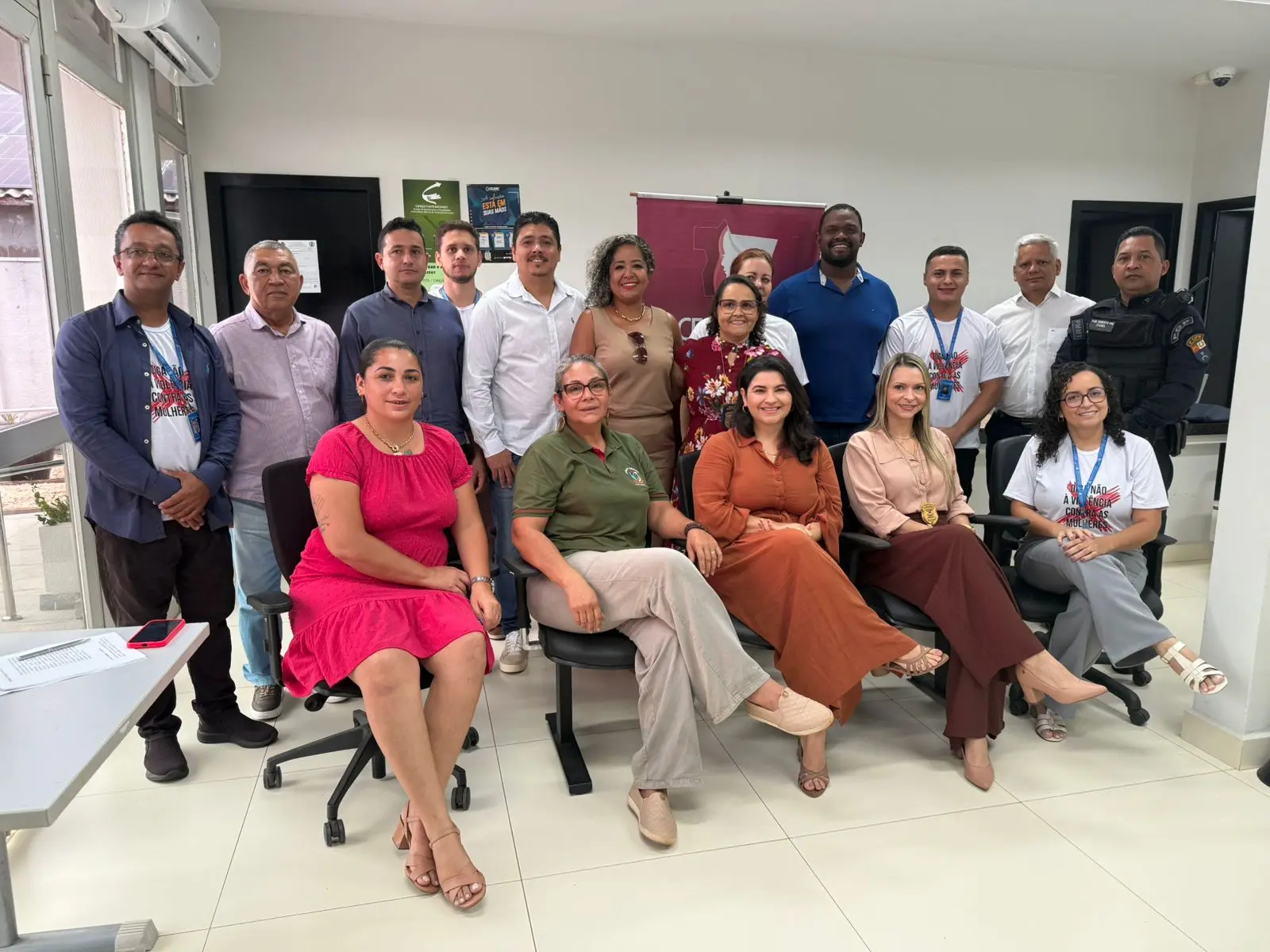 Grupo heterogêneo de servidores, autoridades e integrantes da rede posa em sala ampla e iluminada. Todos estão sorrindo, alguns sentados e outros em pé, com o banner do CEMULHER ao fundo, marcando o encontro em Nortelândia.