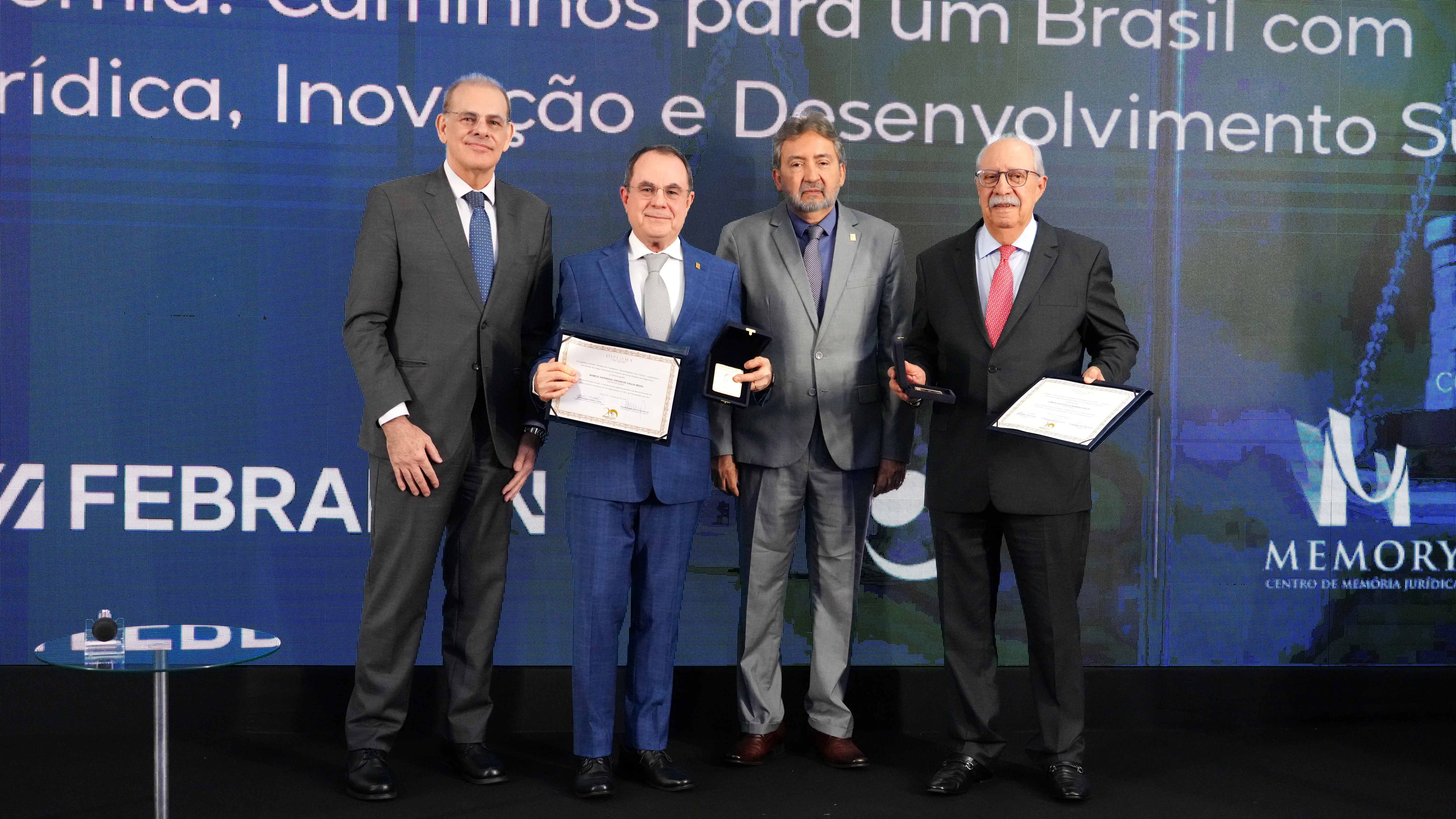 fotografia colorida de um grupo de pessoas em pé, em um palco, segurando diplomas.