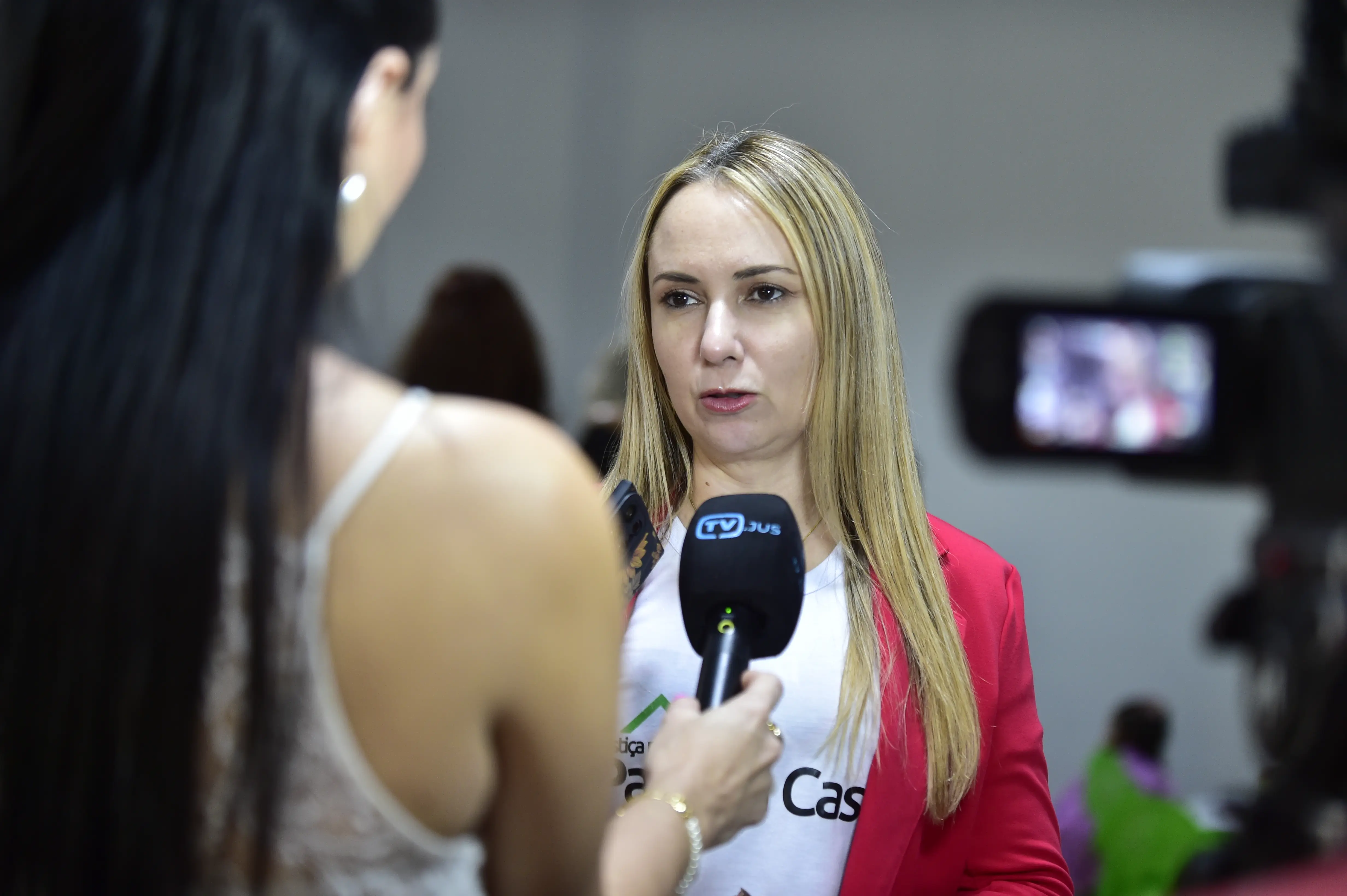 A imagem mostra a juíza Ana Graziela, uma mulher branca, com cabelos lisos e loiros. Ela fala ao microfone da TV Justiça. É possivel ver a repórter de costas, ela tem cabelos longos, lisos e escuros. 