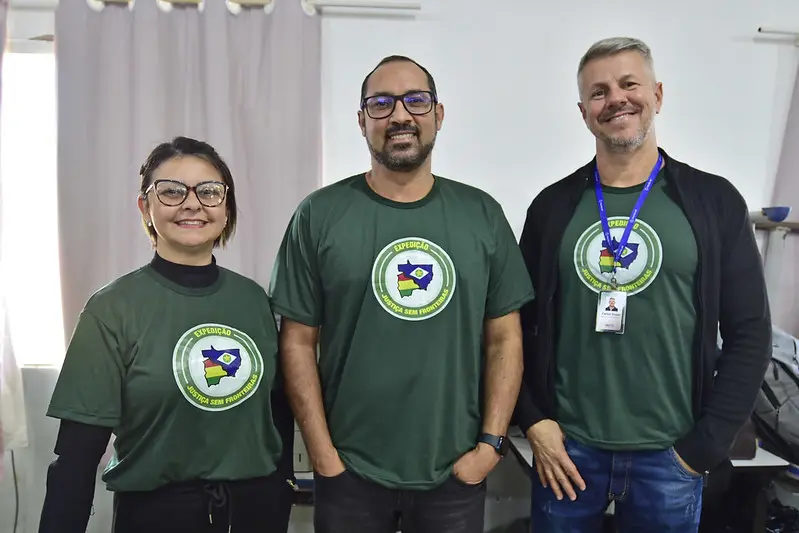 Servidores responsáveis pela emissão de RG posam para a foto, sorrindo. São uma mulher e dois homens, usando a camiseta da Justiça Sem Fronteiras.