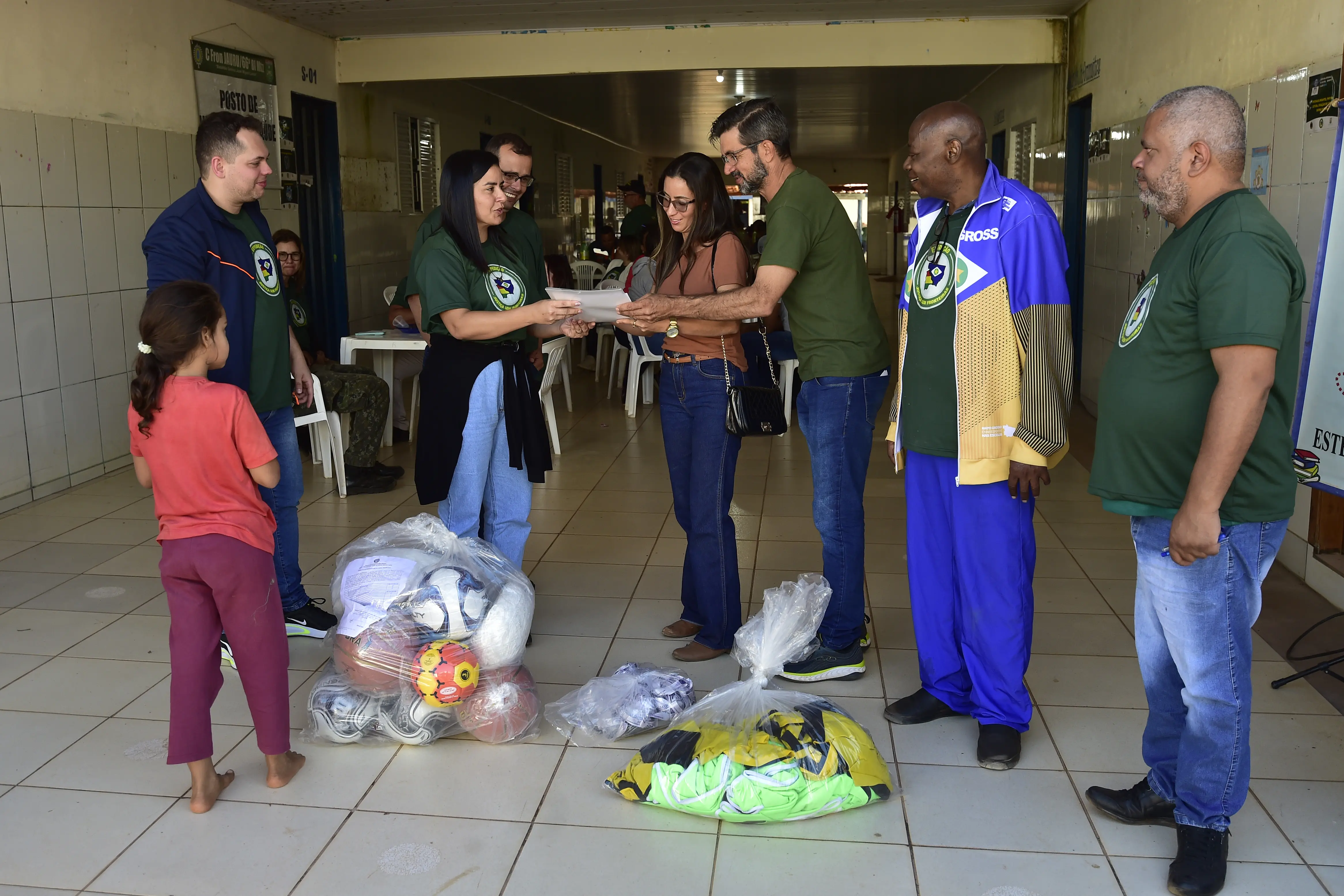 No pátio de uma escola, diretora escolar recebe doação de kits esportivos dos servidores da Secretaria de Estado de Esporte.