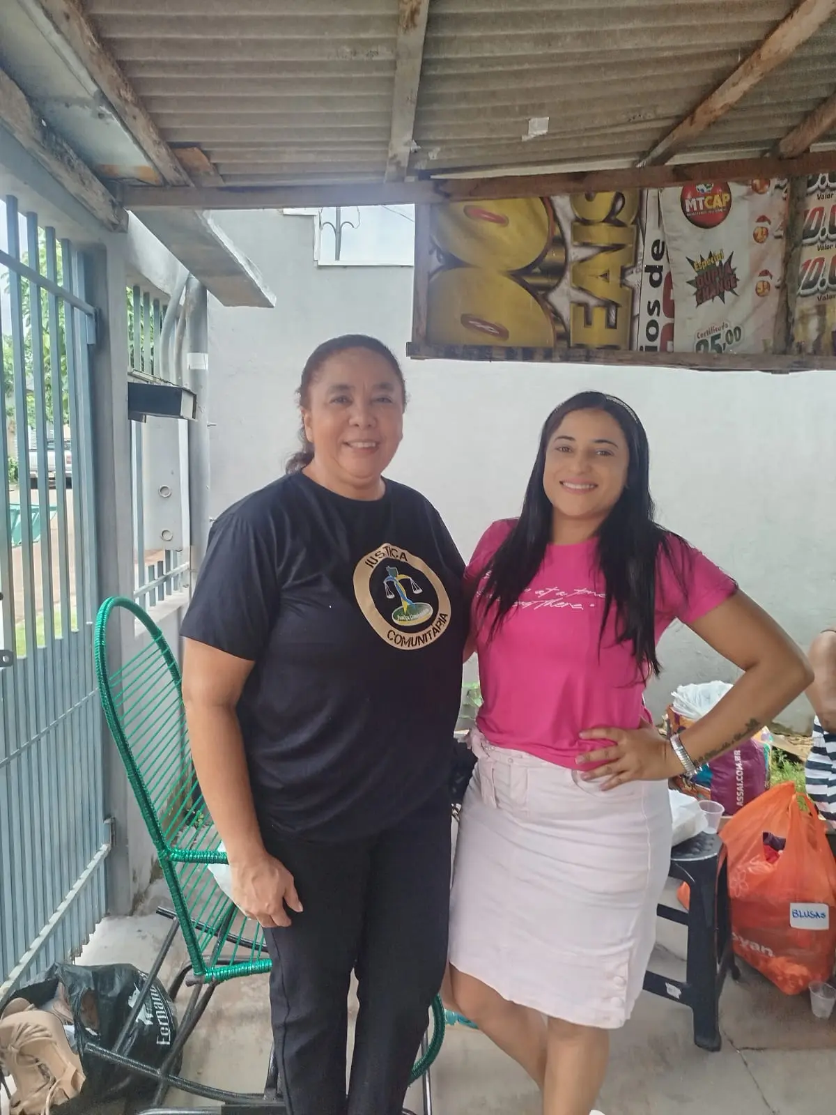 Duas mulheres posam próximas a doações organizadas, em espaço simples e coberto. A cena evidencia parceria, acolhimento e compromisso com ações solidárias.