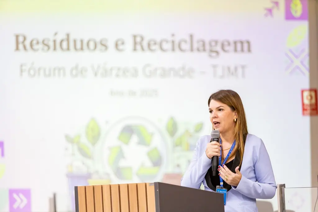Foto na horizontal que mostra a gestora do Núcleo de Sustentabilidade do TJMT, Jaqueline Schofen, falando ao microfone. Ela é uma mulher branca, loira, usando blazer lilás.