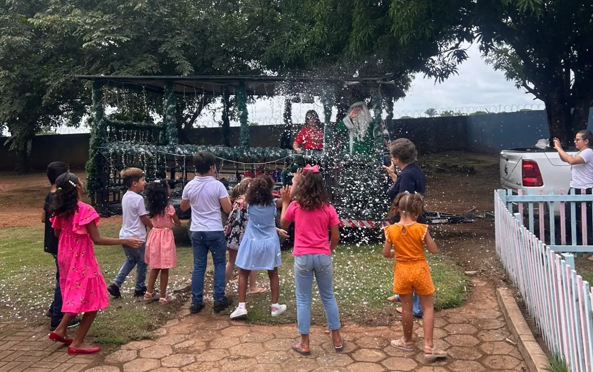 crianças e adolescentes participam de atividade recreativa ao ar livre durante a festa de Natal, com brincadeira de espuma e presença do Papai Noel.
