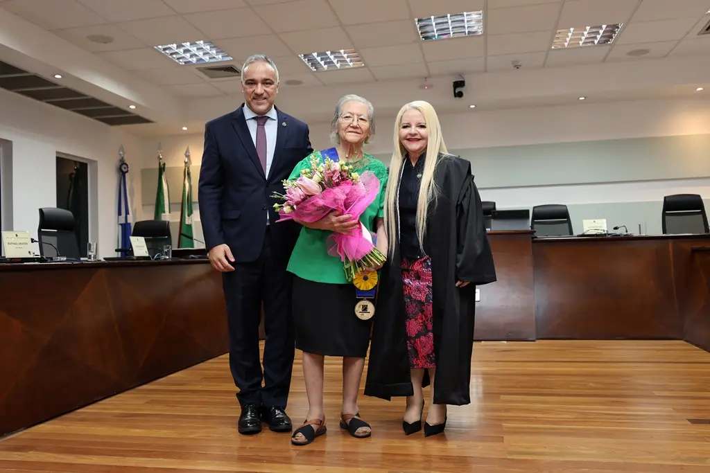 Foto que mostra o diretor da Escola Judiciária Eleitoral, Welder Queiroz; a desembargadora aposentada Shelma Lombardi de Kato e a presidente do TRE/MT, desembargadora Serly Marcondes Alves, posando juntos para a foto e sorrindo, no Plenário do TRE. 