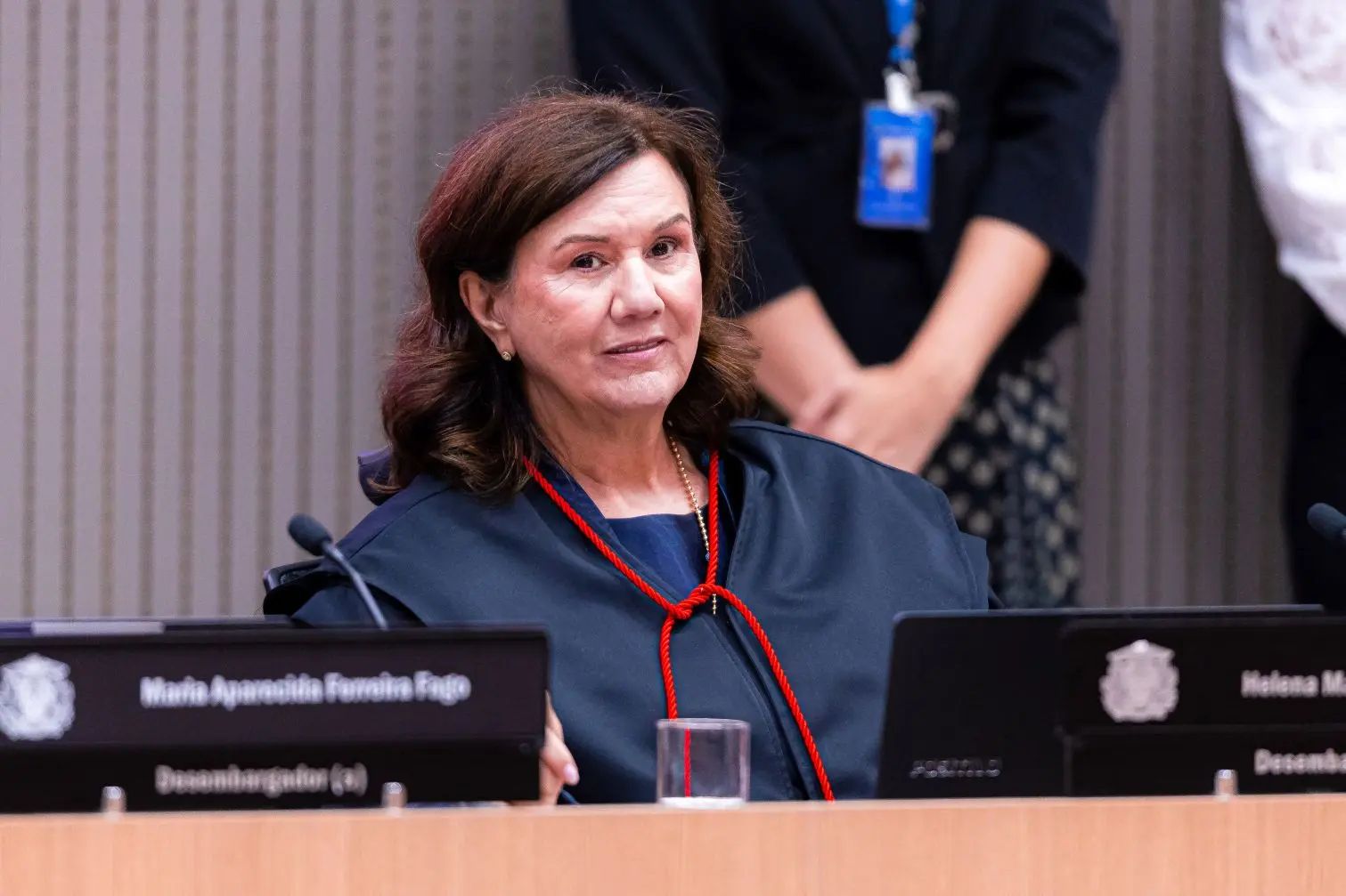 Foto horizontal que mostra a desembargadora Helena Maria Bezerra Ramos sentada na mesa do Plenário 1 do TJMT. Ela é uma mulher branca, de olhos castanhos, cabelos castanhos, lisos, na altura dos ombros, usando toga.