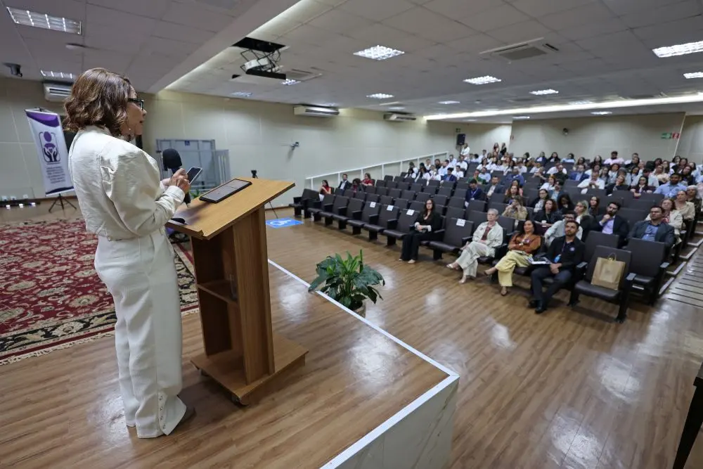 Foto horizontal colorida que mostra a desembargadora Juanita Clait Duarte falando ao microfone, no púlpito do auditório do TJMT, de frente para a plateia sentada. 