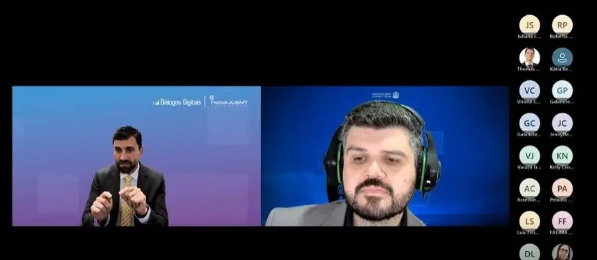 Tela de reunião virtual mostra juiz Vinícius falando e gesticulando durante apresentação no Diálogos Digitais. Ao lado, o servidor Thales usa fone de ouvido e acompanha atentamente. Fundo institucional do TJMT e InovaJusMT.