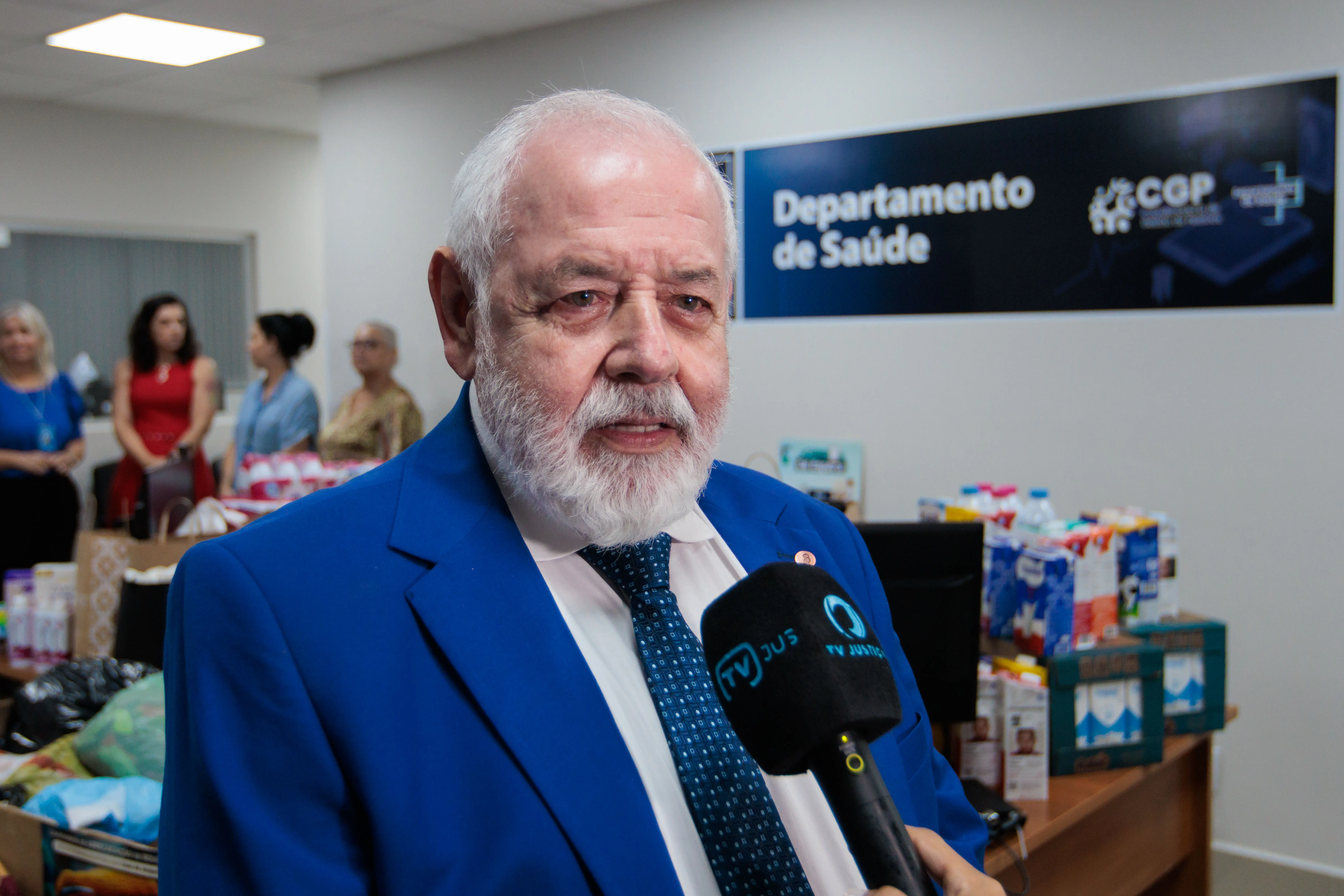 Presidente José Zuquim em ângulo fechado. Ele é um homem branco, de barba e cabelos brancos, usa blaser azul, gravata azul e camisa branca