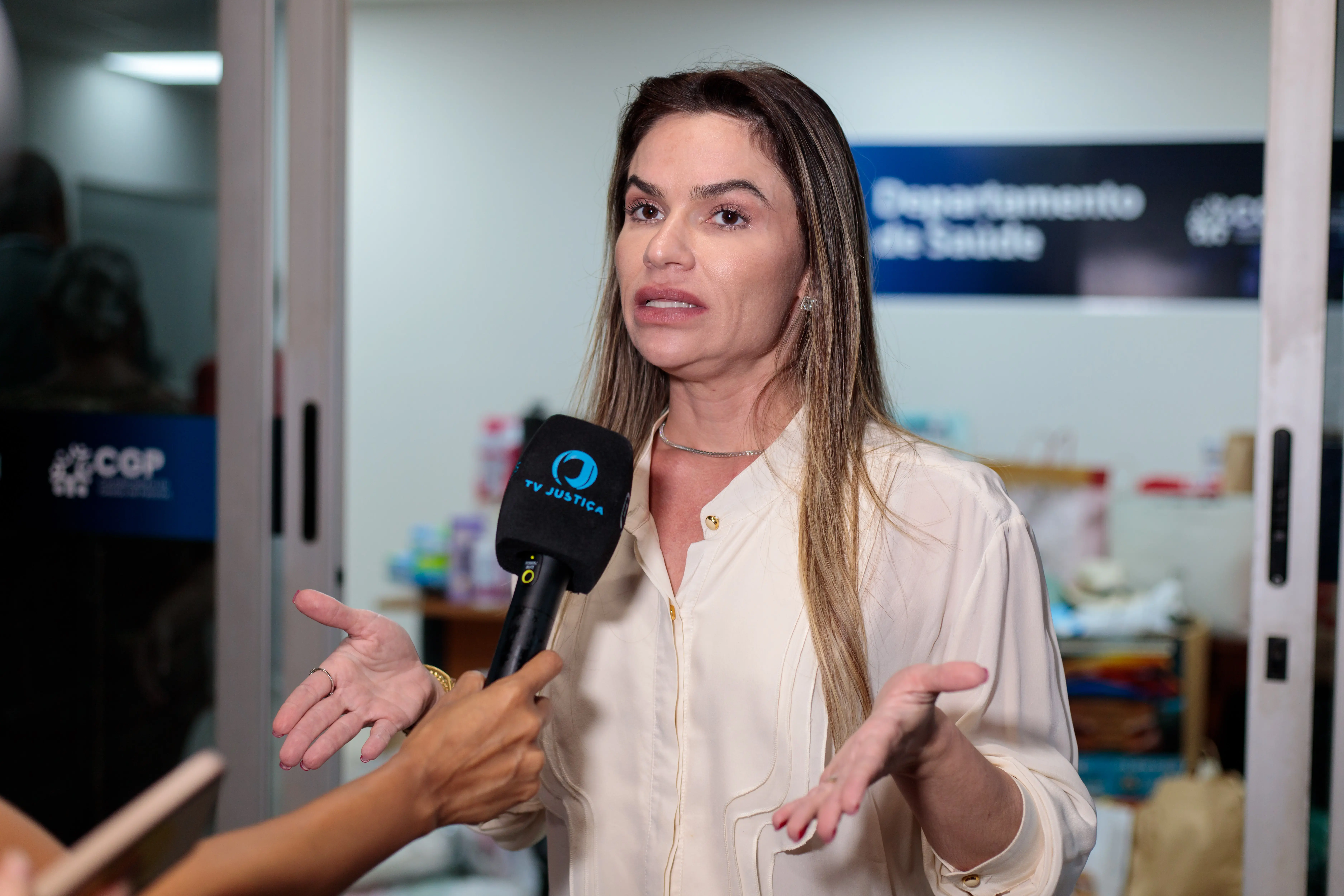 Advogada Aline concede entrevista durante doação de roupas para Casa de Amparo. Ela é um a mulher magra, branca, de cabelos compridos loiros e usa uma camisa de manga comprida bege