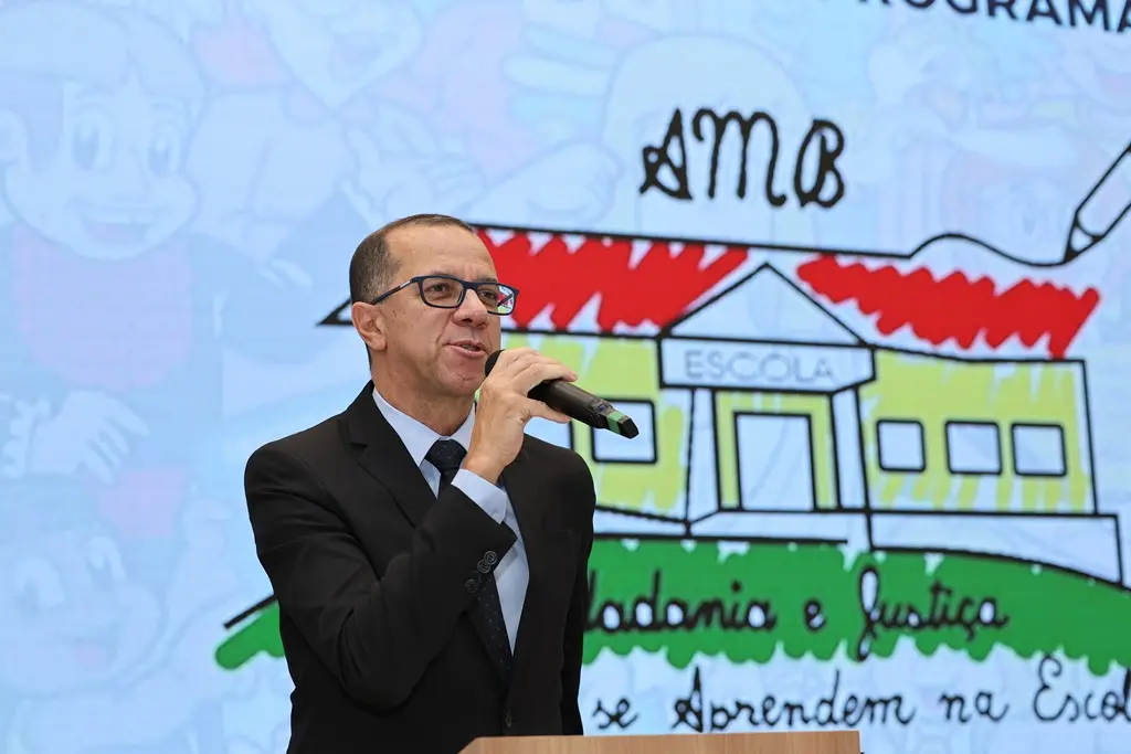 Secretário da AMB, juiz Carlos Martins fala ao microfone. Atrás dele, há um telão com a logomarca do programa Justiça e Cidadania.