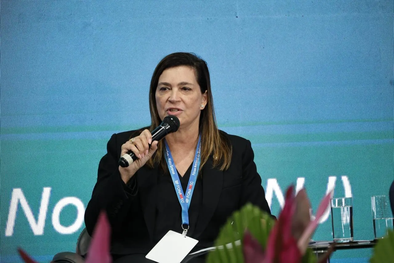 Conselheira do CNJ Mônica Autran Machado sentada, falando ao microfone. Ela é uma mulher branca, de cabelos lisos e castanhos, usando camisa e blazer pretos e crachá do evento.